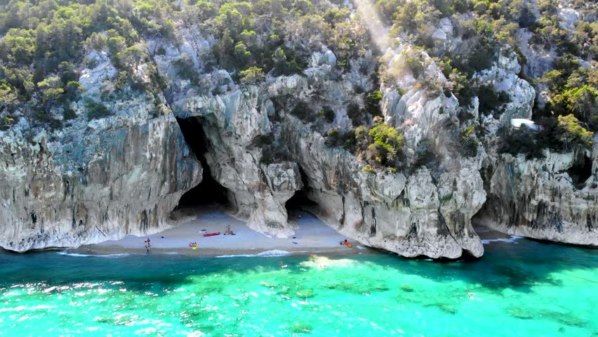 Cala Luna in Sardinia, Italy showcases stunning cliffs and turquoise waters perfect for a relaxing holiday. Visitors enjoy the serene beach, sunbathing, and swimming in a picturesque setting.