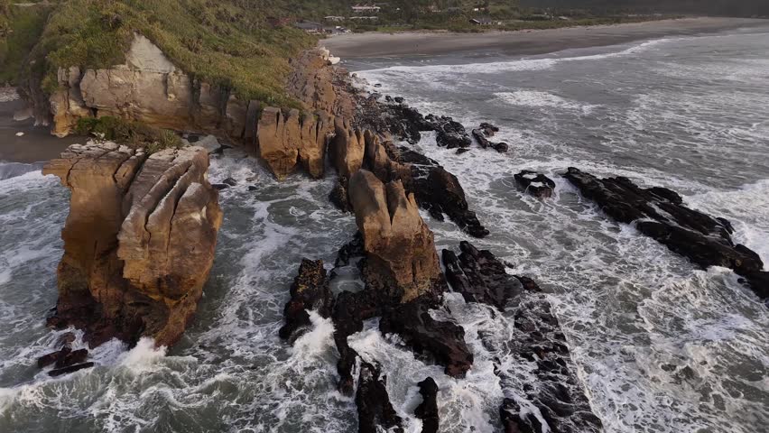 Aerial sunset view of Pancake Rocks in Punakaiki on New Zealand West Coast. Waves crash on layered limestone formations under golden skies
