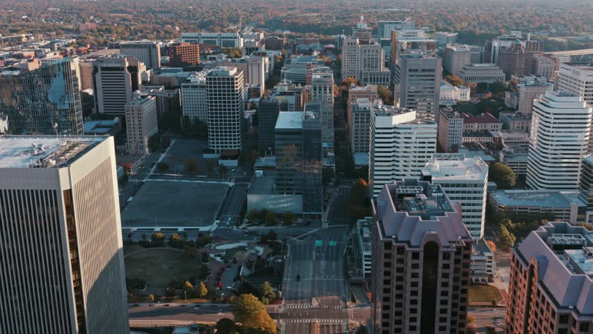 High angle aerial drone view of downtown Richmond showing office towers, streets, and urban grid under warm golden hour light with clear sky and expansive cityscape