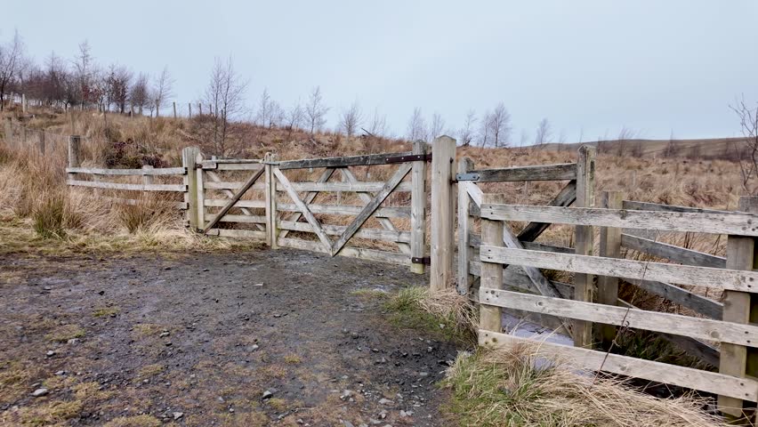 Rustic wooden gate and fence stretching across a dry grassy field on a cloudy day