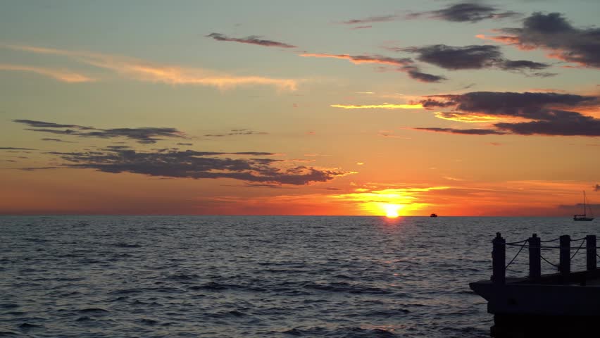 Standing on a pier and watching the beautiful and romantic sunset. The sky is gold and the water of the ocean moves calmly.