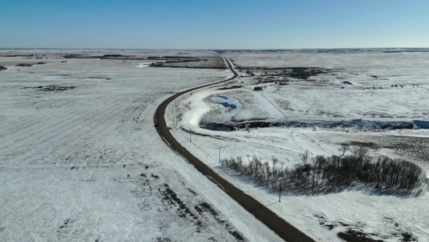 Push in aerial drone shot in small town Saskatchewan rural farmland, following a quite dirt road through the prairies.