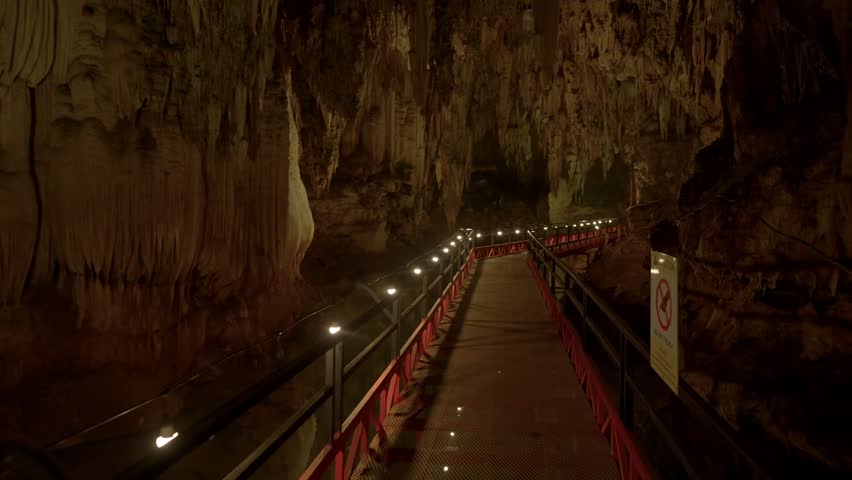 Camera pushes forward and looks up at a stalactite before tilting down to show the walkway again.
