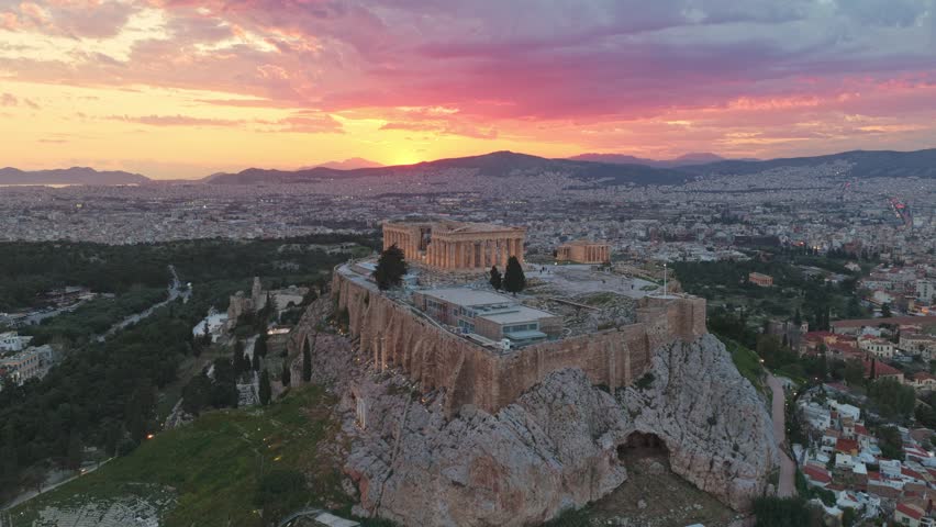 Aerial view of the famous acropolis of athens and the parthenon temple with a dramatic and colorful sunset sky, showing the ancient citadel overlooking the sprawling cityscape of greece