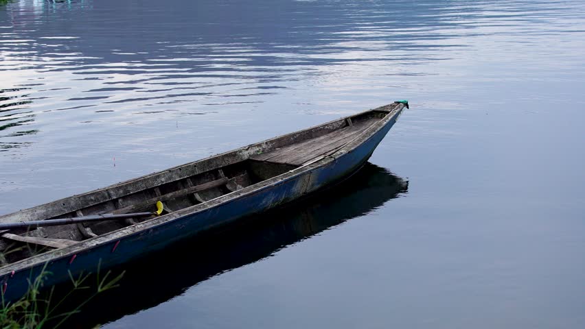 Old weathered wooden canoe moored on the calm waters of Selorejo Reservoir, Indonesia, featuring ample negative space on the right for text or design copy.