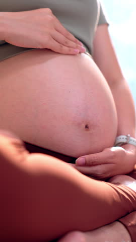 Vertical close up expectant mother peacefully relaxing outdoors holding exposed pregnant belly warm sunlight showing deep maternal love and joyful anticipation for new baby arriving soon VERTICAL