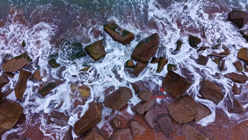 Waves move over large rocks at the shore while water splashes against them. The scene shows a view of the coast where the sea meets land in the afternoon light.