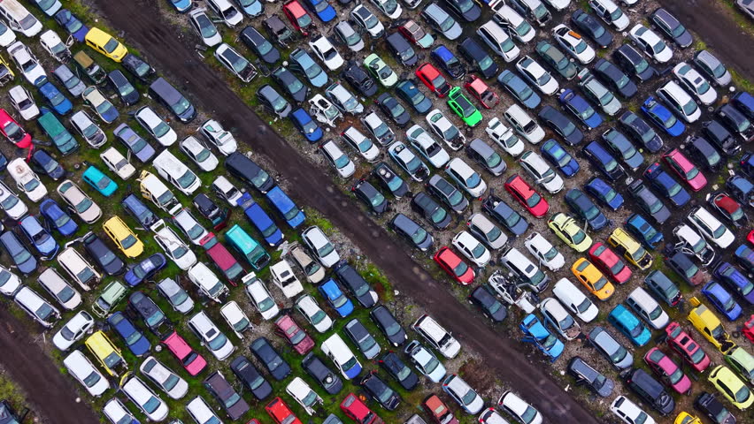 Large area filled with parked cars of different colors, arranged in tight rows. The scene shows a lot with vehicles under a clear sky, highlighting their variety and arrangement.