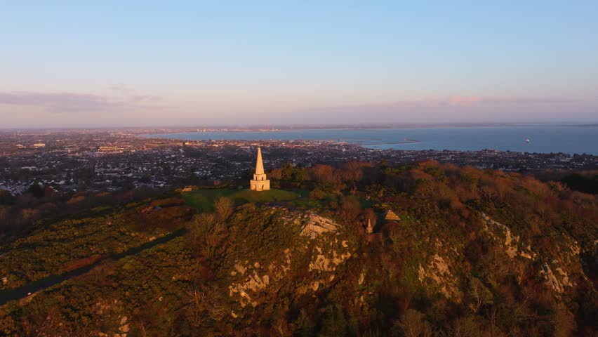The obelisk on Killiney Hill stands against a sunrise backdrop, overlooking Dublin Bay and the city. Ideal for use in travel, tourism, or landscape projects.