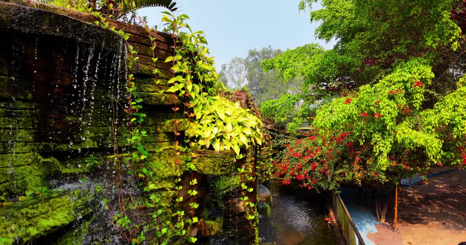 Lush Green Waterfall Garden with Red Flowers and Natural Stone Landscape Background