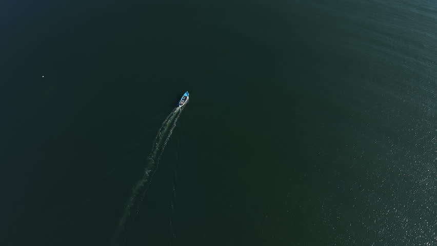 A boat moves through the ocean, creating a wake in the water. The sun shines brightly, reflecting on the surface. The view shows the vast expanse of water nearby.