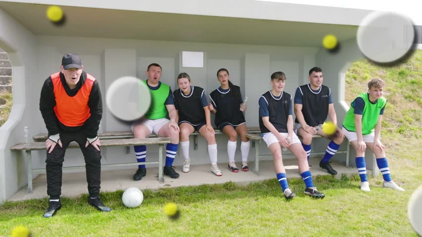 Soccer team and coach on bench reacting to play, shifting, shouting, blurred discs obscuring view. Players, sideline, pitch, bibs, bottle, vibrant, teamwork