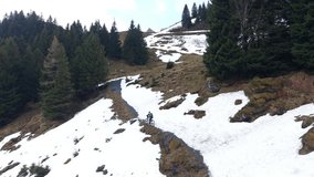Drone static shot of a cyclist continuing uphill after passing a snowy section, riding away on a partially clear mountain road - Powered by Shutterstock - Get 15% off with code: PIKWIZARD15