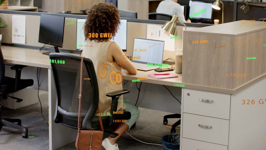 Woman typing on laptop in office, gesturing for papers, initiating animated business data overlays. Colleagues, computer, desk, monitor, plants, lamp, document