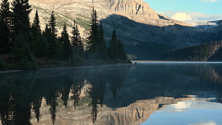 View across a calm mountain lake surrounded by dense evergreen trees in a peaceful alpine wilderness landscape scene.