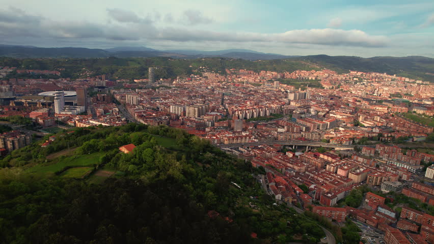 Aerial drone view of Bilbao at sunset with skyline, neighborhoods and warm golden light. Scenic urban landscape in Basque Country, northern Spain. High quality 4k footage