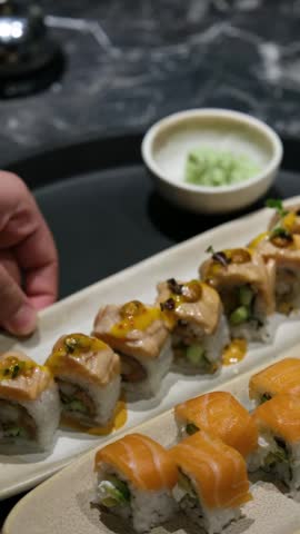 Static close up shot of a colorful and appetizing sushi platter featuring premium salmon nigiri and uramaki rolls with ginger and wasabi on a white ceramic plate in a blurred restaurant background for digital food delivery app menus and restaurant website headers