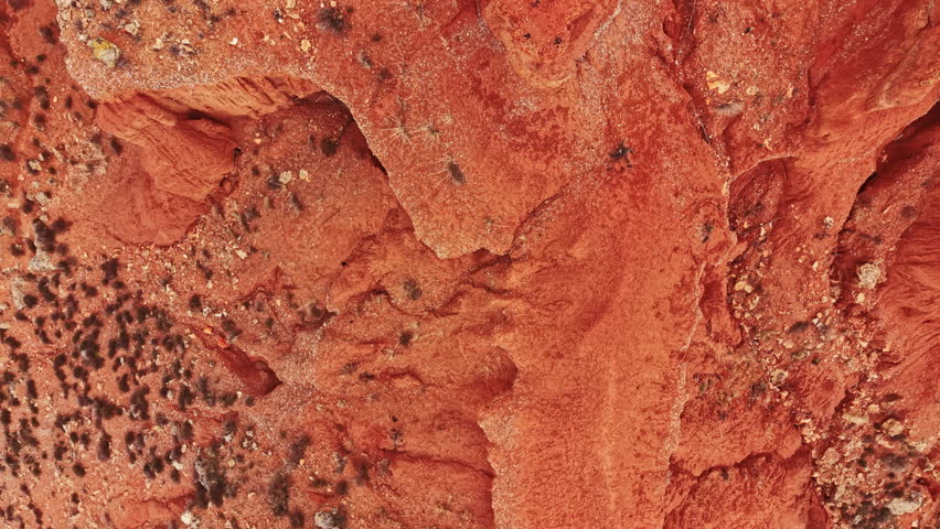 Vast canyon landscape shows red rock formations and dry earth. The view highlights the texture and details of the ground under bright daylight.