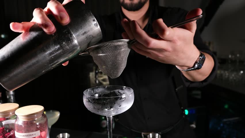 Close up of a bartender pouring a pink frothy cocktail into a coupe glass with precision focusing on the smooth texture and professional technique for gourmet beverage promotional videos
