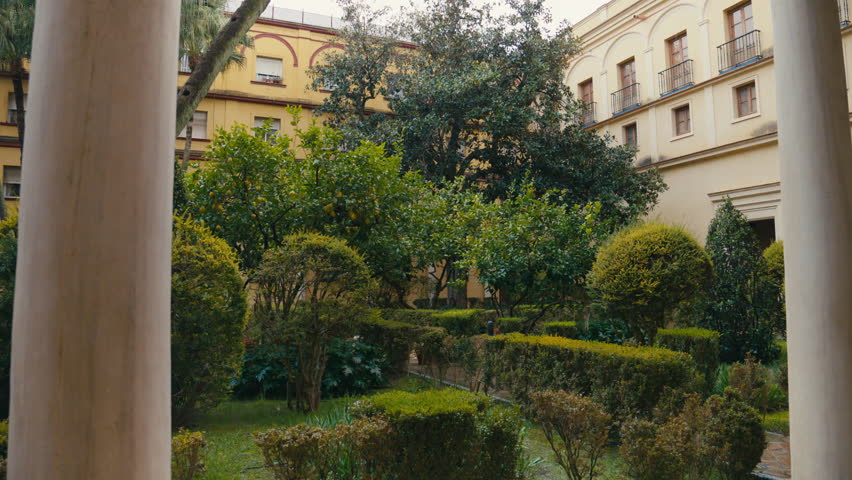 Peaceful garden courtyard in Seville, Spain, featuring lush greenery, orange trees, and traditional architecture creating a calm Mediterranean atmosphere.