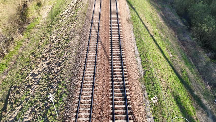 Train tracks stretch into the distance through a lush green landscape, showcasing the gradual transition of scenery along the railway corridor under a clear blue sky