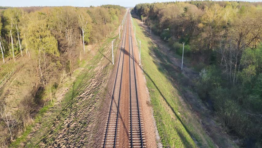 Train tracks stretch into the distance through a lush green landscape, showcasing the gradual transition of scenery along the railway corridor under a clear blue sky