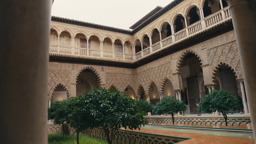 View of a historic courtyard inside Real Alcázar in Seville, Spain, featuring intricate Moorish architecture, ornate arches, and a lush central garden.