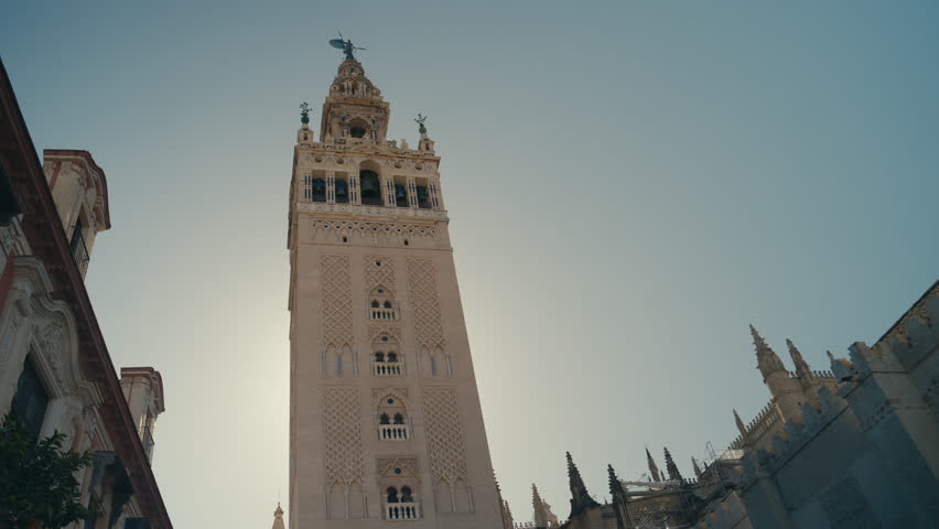 Low angle view of La Giralda, the iconic bell tower of Seville Cathedral in Spain, showcasing historic architecture, intricate details, and clear sky above.