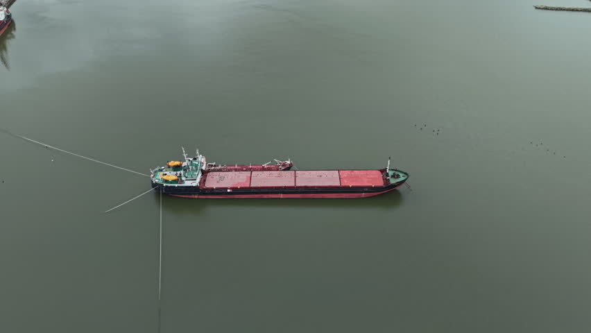A cargo ship is anchored in a river. Other boats can be seen in the background. The scene captures the daily activity of shipping and transportation. The sky is clear and bright.