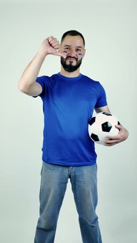 Upset soccer supporter with a blue painted face holding a ball and showing a thumbs down gesture