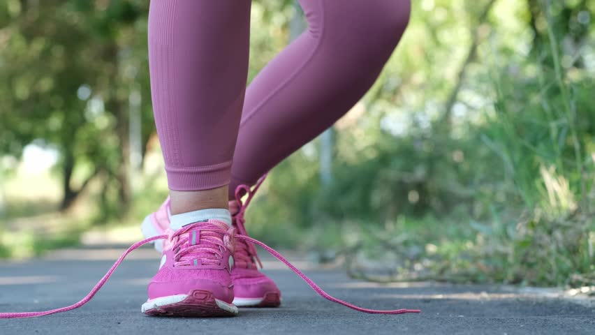 Female runner tying shoelaces on running shoes for a summer jog close up. Concept of preparation, sport, motivation, and healthy lifestyle
