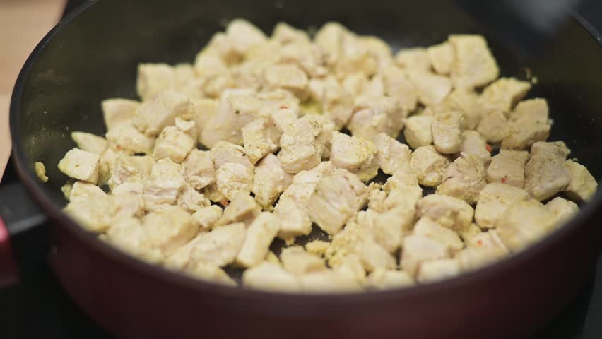 Chunks of chicken are being cooked in a skillet with regular stirring to ensure even cooking and flavor absorption.