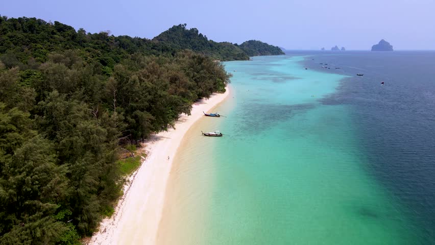 A turqouse colored ocean with clear water at Koh Kradan, a tropical island in Trang, Thailand, and a coral reef in front of a tropical island