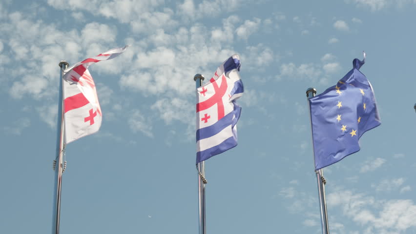 Flags of Europe, Georgia and Autonomous Republic of Adjara flutter against background clear blue sky with clouds