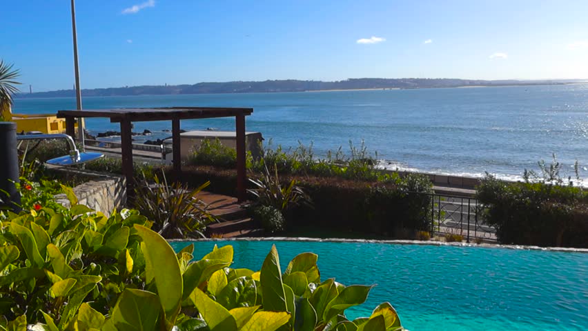 Serene infinity swimming pool at a luxury hotel resort overlooking the sparkling Atlantic Ocean on a sunny day in Portugal, offering a tranquil and exclusive vacation experience