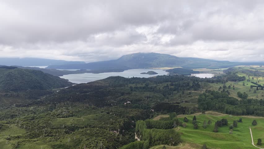 Wide aerial view of Waimangu Volcanic Valley under dramatic cloudy sky with lakes and rolling hills in New Zealand.