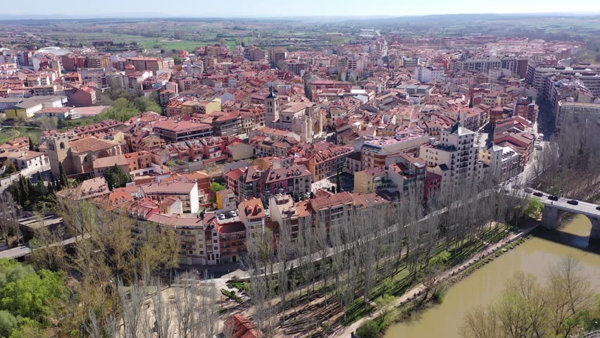 Scenic drone view of modern residential areas of Aranda de Duero city on banks of Duero river on sunny spring day on background of natural rural landscape, Burgos, Spain