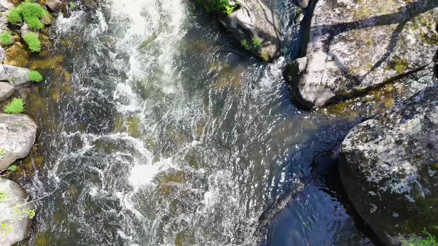 Crystal clear water flowing downstream over large rocks and boulders in a pristine mountain river. Scenic top down view of a wild creek