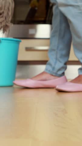 Vertical video: Woman cleaning kitchen floor mop motion sparking growing social likes around feet. Minimalist, domestic, slippers, bucket, turquoise, wooden, vertical video