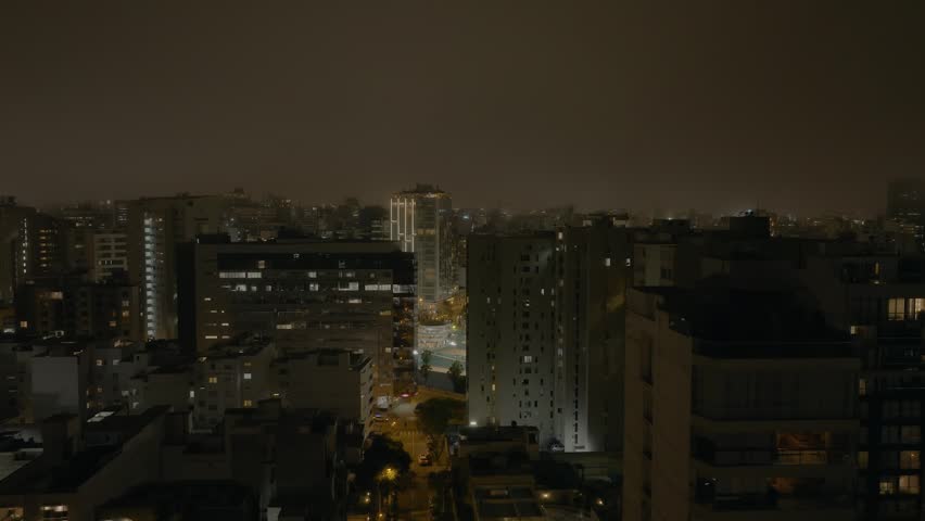 Night aerial view of Miraflores district in Lima, Peru, showcasing illuminated buildings, coastal lights, and vibrant urban life along the Pacific Ocean. Modern cityscape at night.