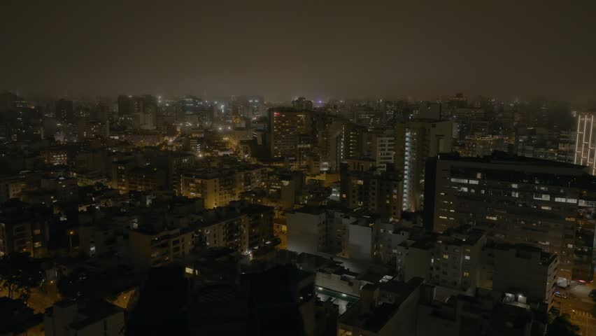 Night aerial view of Miraflores district in Lima, Peru, showcasing illuminated buildings, coastal lights, and vibrant urban life along the Pacific Ocean. Modern cityscape at night.
