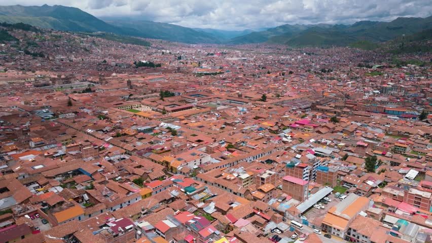 Drone aerial view of the historic center of Cusco, Peru, featuring colonial architecture, red tiled rooftops, and Andean mountain surroundings. UNESCO World Heritage Site.