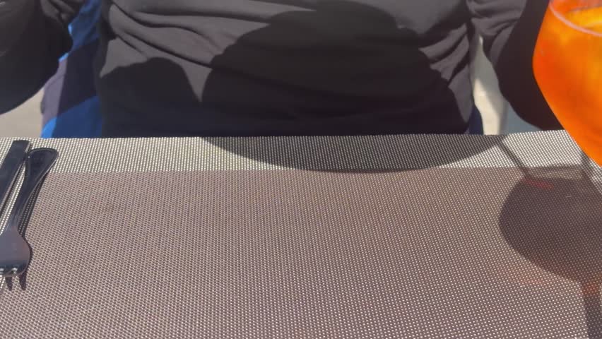 Adult diner eating creamy salmon pasta with lemon slices at an outdoor restaurant table on a sunny day.