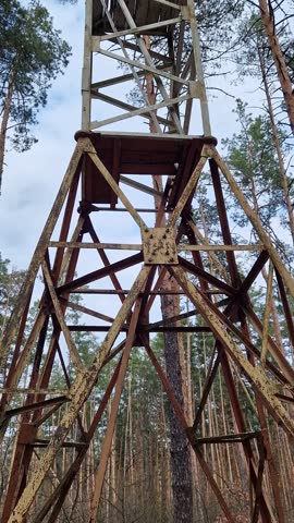 Old fire watchtower in the forest against a blue sky. High metal structure of an abandoned forest tower, shot from a lower perspective. Rusty steel tower with an observation deck on top
