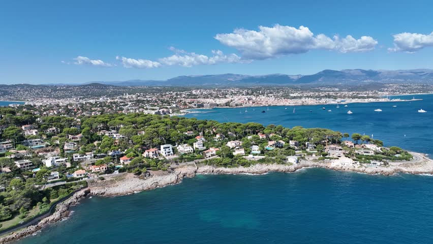 Aerial view of the stunning Antibes coastline, contrasting vibrant green trees with the deep blue sea dotted with white boats, Antibes, France.