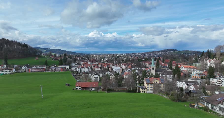 Aerial view of the city, where buildings with red roofs stand out against the green fields and rolling hills, St. Gallen, Switzerland.