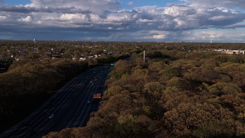 Aerial hyper lapse gliding over green trees in Valley Stream State Park on a sunny day. The camera boom up and truck right then tilt up to reveal the blue sky and dark clouds.