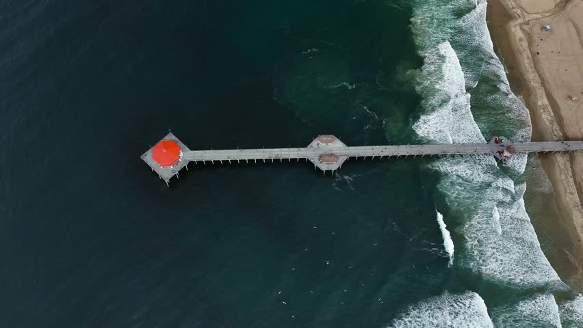Aerial view of Huntington Beach Pier stretching out into the dark turquoise ocean waters with sandy beach on the right, Huntington Beach, California, United States.