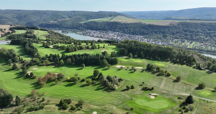 Aerial view of the sprawling green Golfclub Jakobsberg beside the flowing river, a vibrant contrast to the distant town, Marksburg Braubach, Germany.