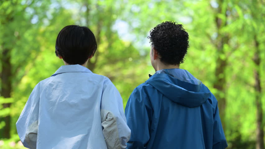 A middle-aged Japanese couple enjoying sports such as walking and running in a park with beautiful fresh greenery. A full-body video conveying a healthy lifestyle and healthcare image. Slow-motion shot of their backs.